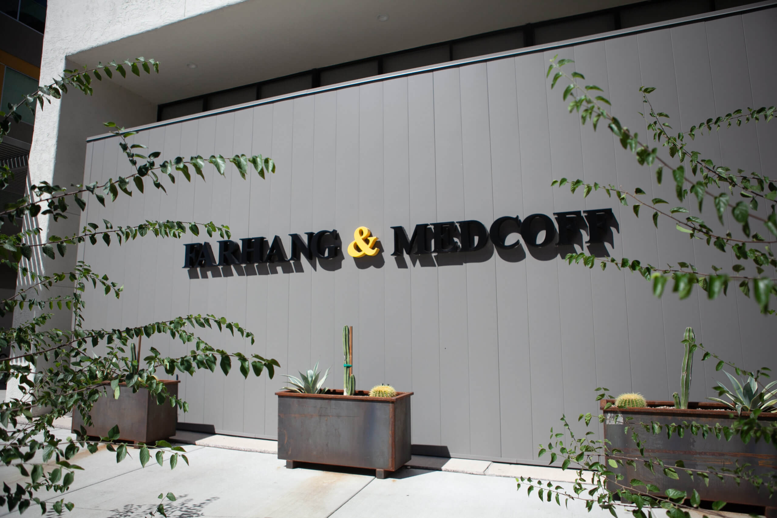 Exterior of a building with a sign reading "Farhang and Medcoff" with three planter boxes containing cactuses